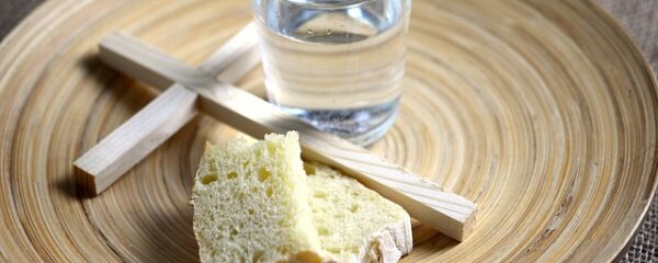 Kreuz, Wasserglas und Brot auf einem Teller